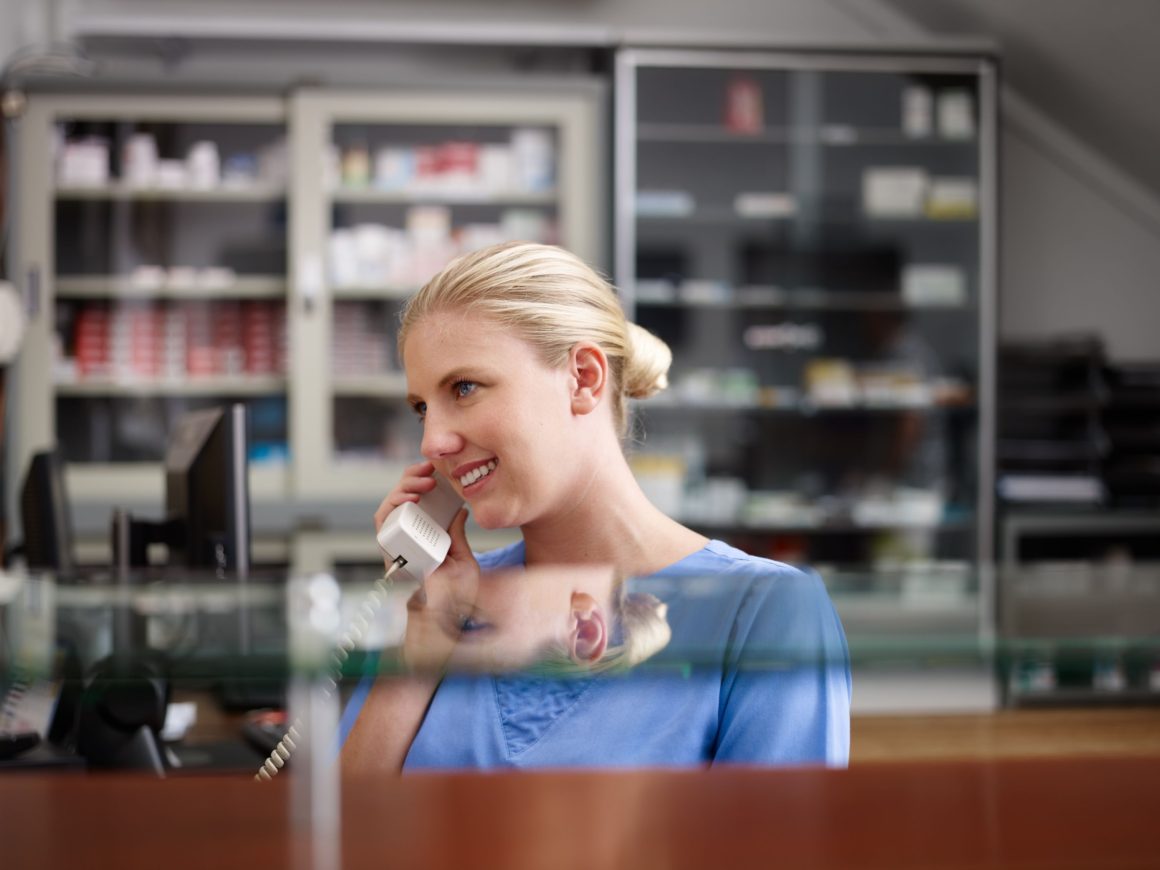 young woman at work as receptionist and nurse in hospital and talking on the phone