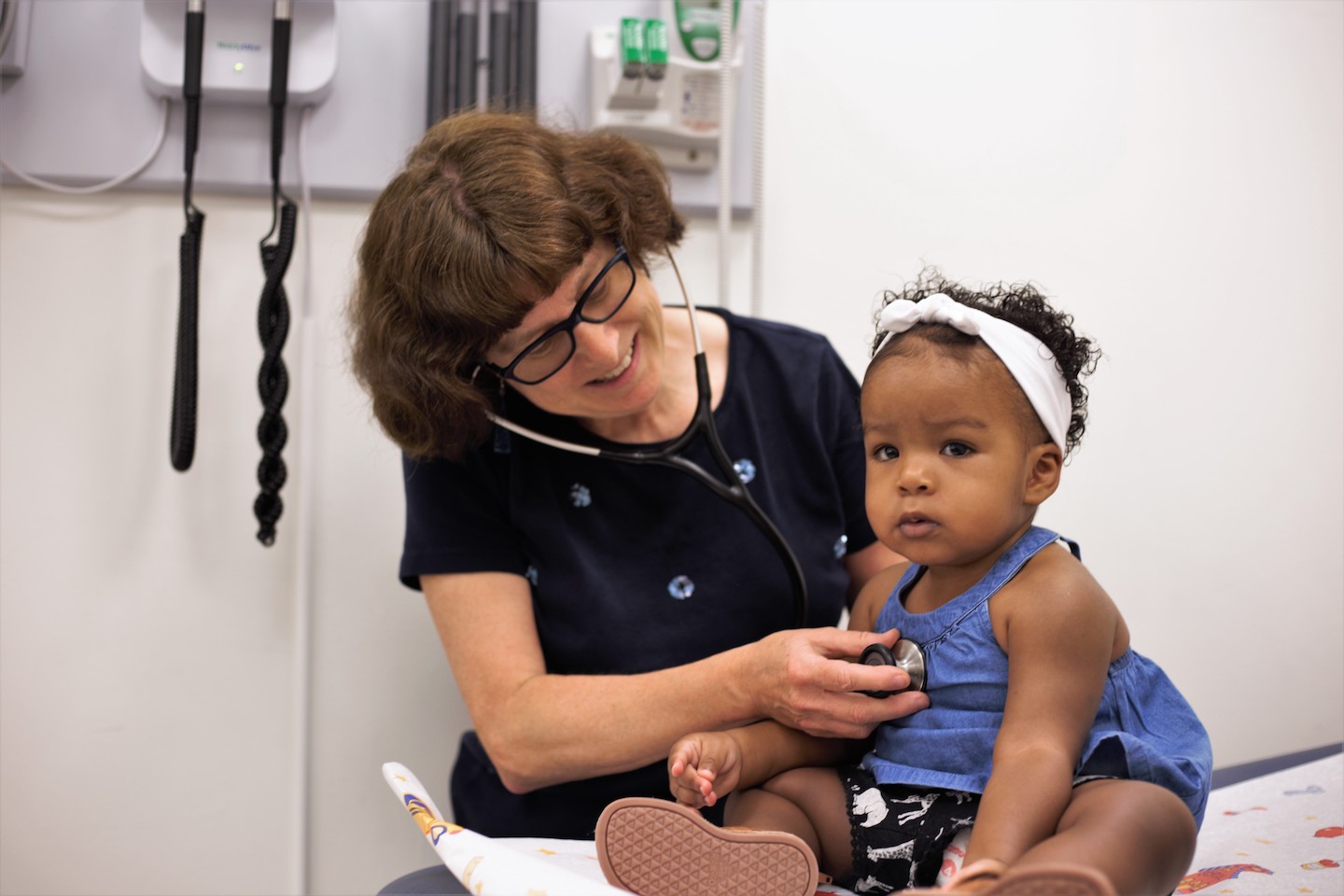 A smiling doctor uses a stethoscope with a toddler.